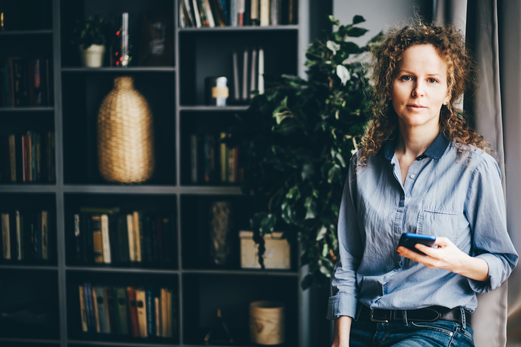 Een vrouw poseert voor een boekenkast met haar telefoon in haar hand