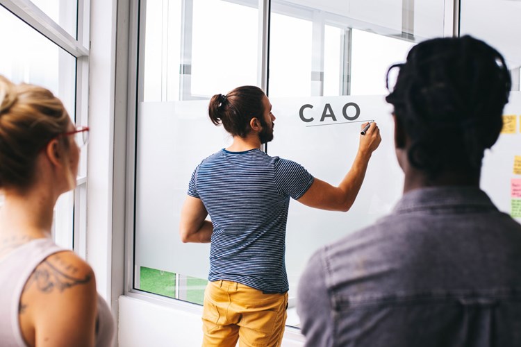 Een man schrijft de het woord CAO op een bord terwijl andere mensen naar hem kijken