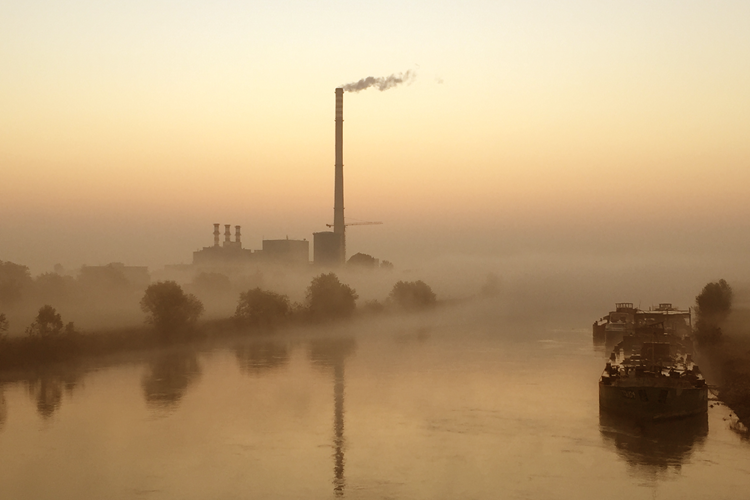 Een mistige rivier met op de achtergrond een fabriek met rokende schoorsteen