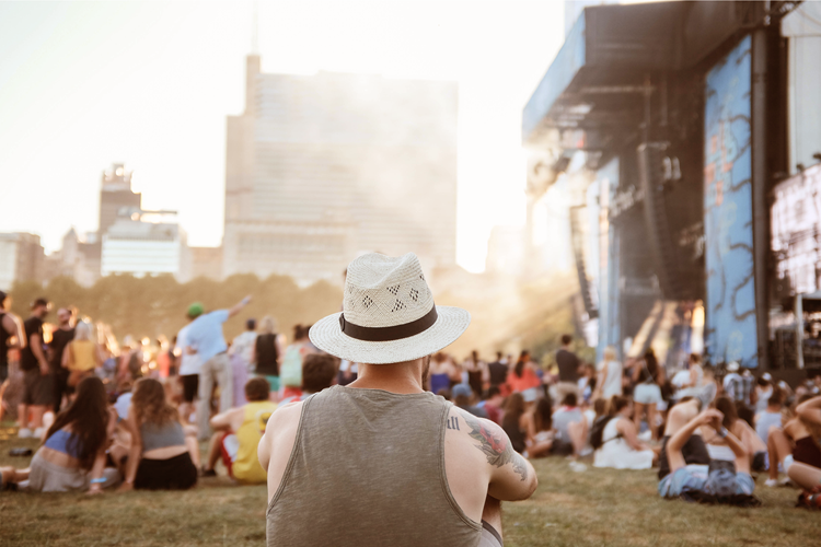 Een man zit op het gras en kijkt naar het podium op een festival