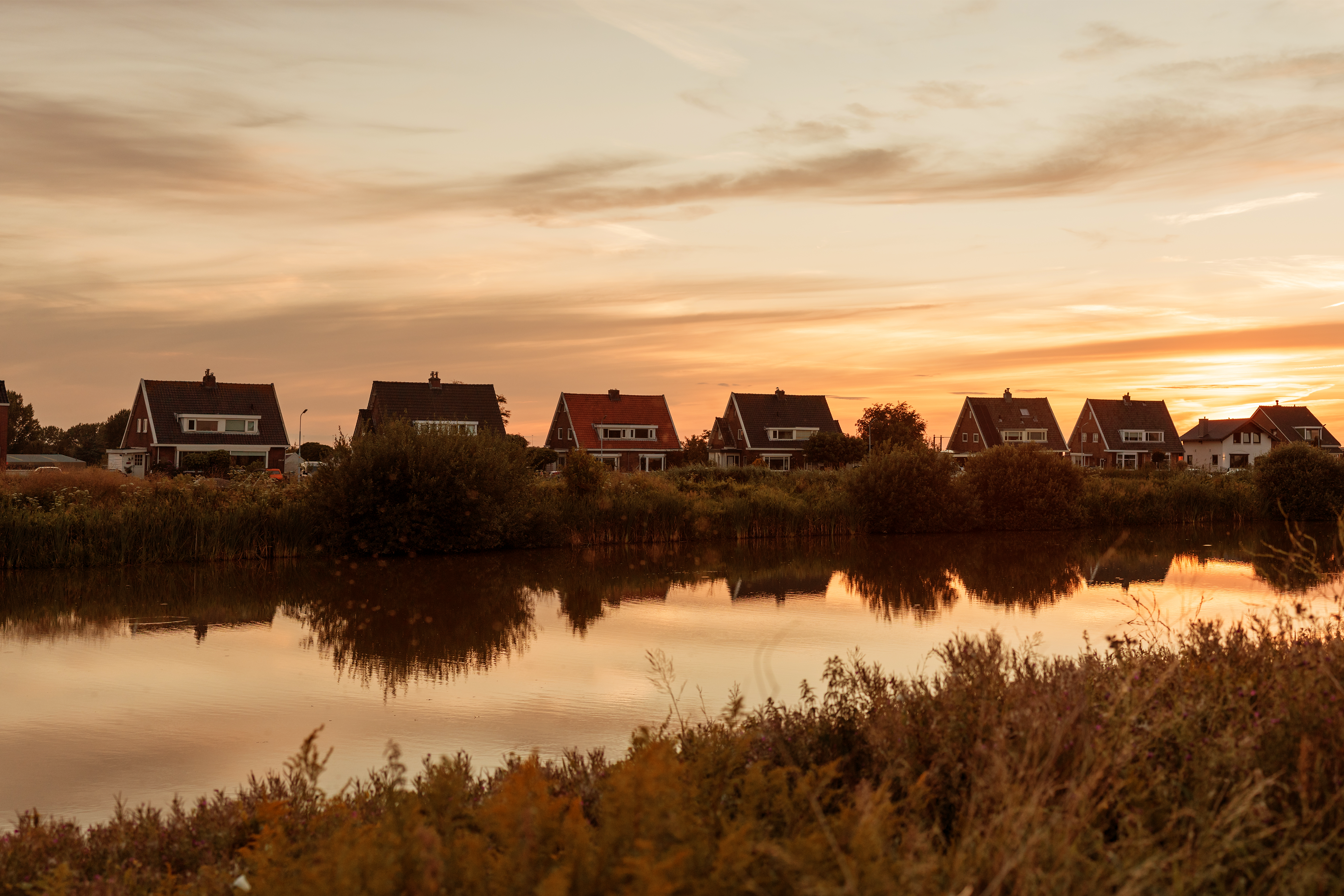 Een rij huizen aan het water bij zonsondergang
