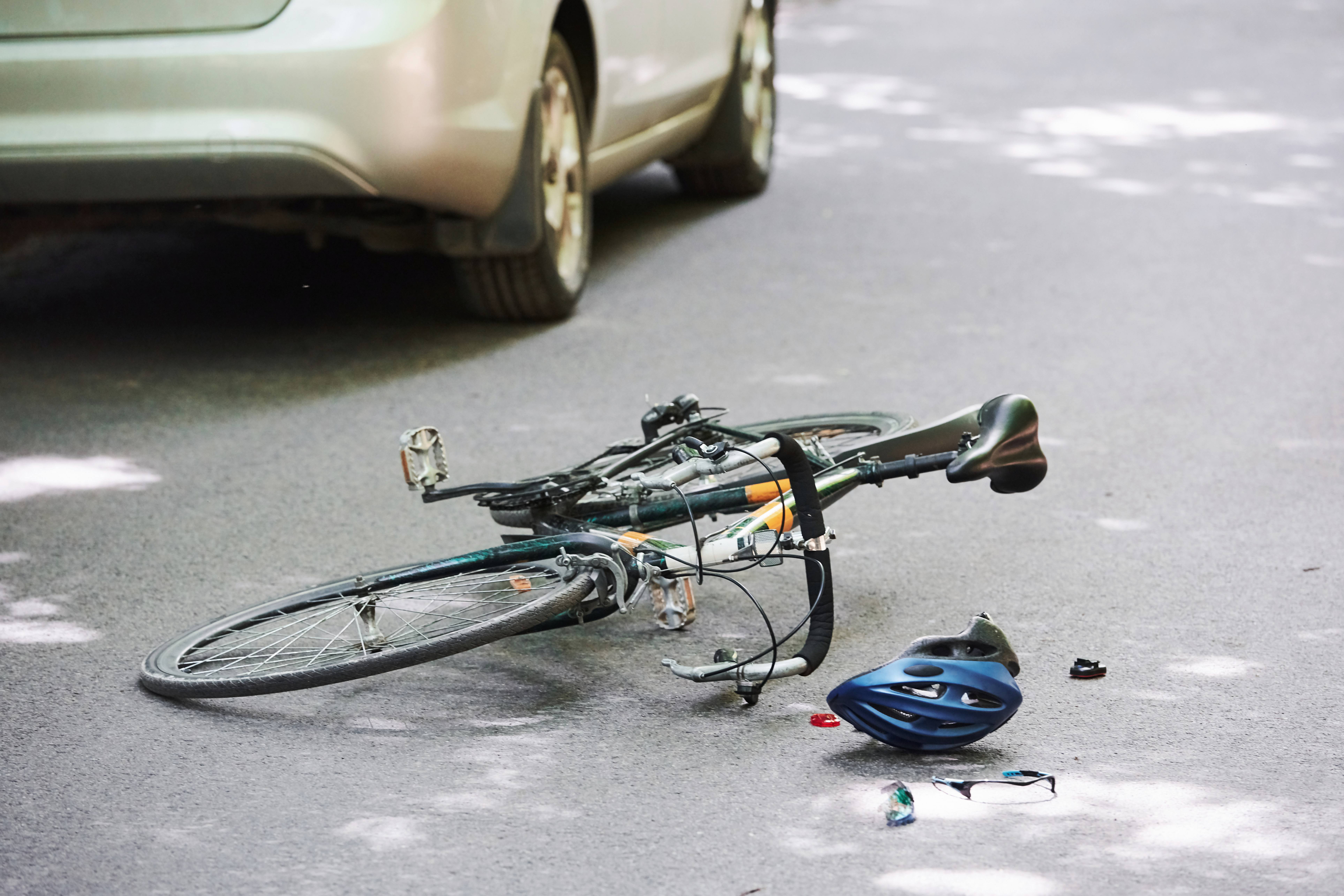 Een kapotte fiets op de grond met een auto ernaast