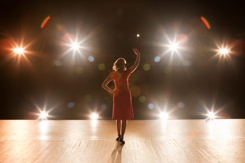 Een vrouw in de spotlight op een podium met haar hand omhoog